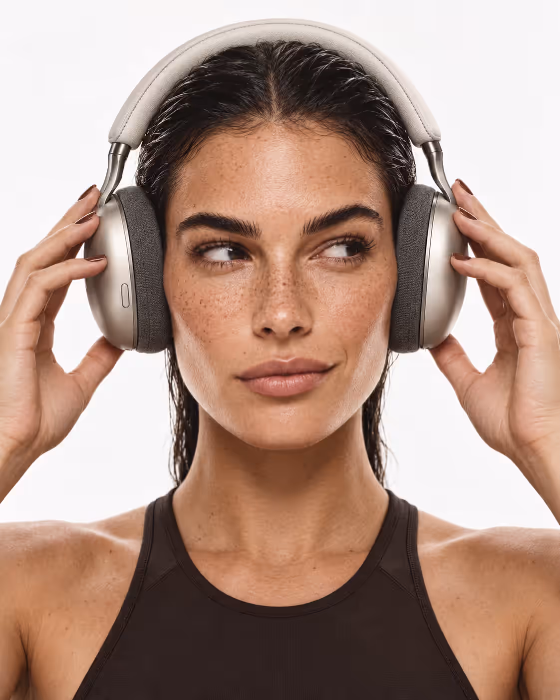 A woman with wet hair holding silver over-ear headphones against a white background