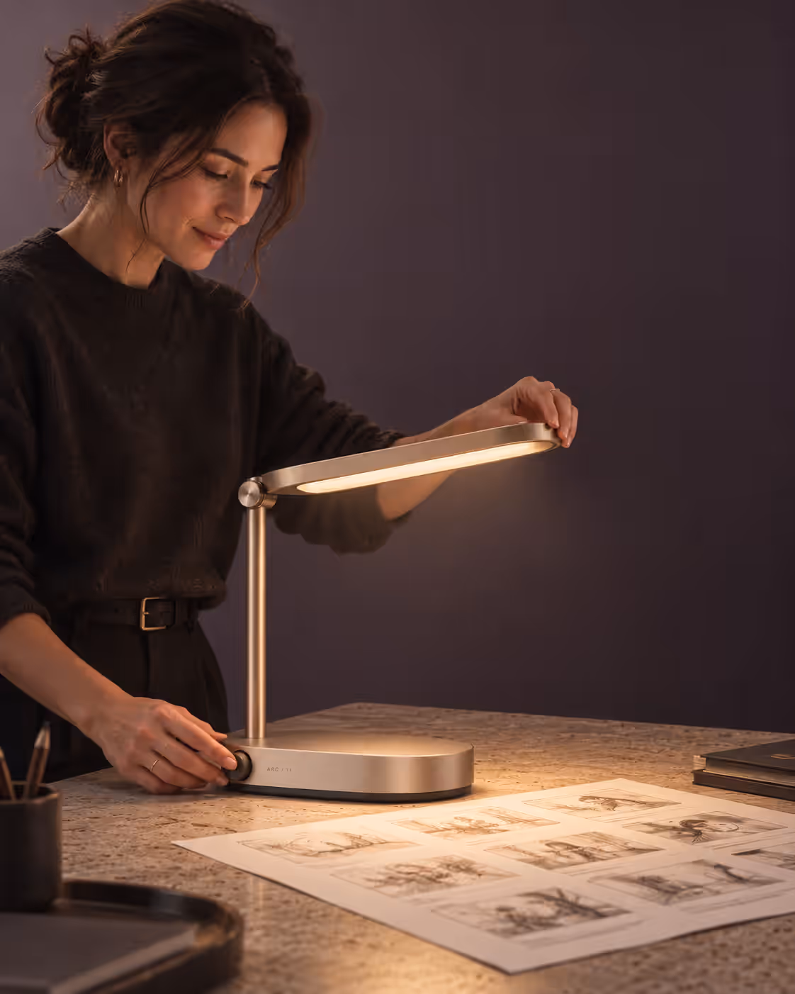 A woman adjusting the desk lamp’s head over a spread of printed contact sheets