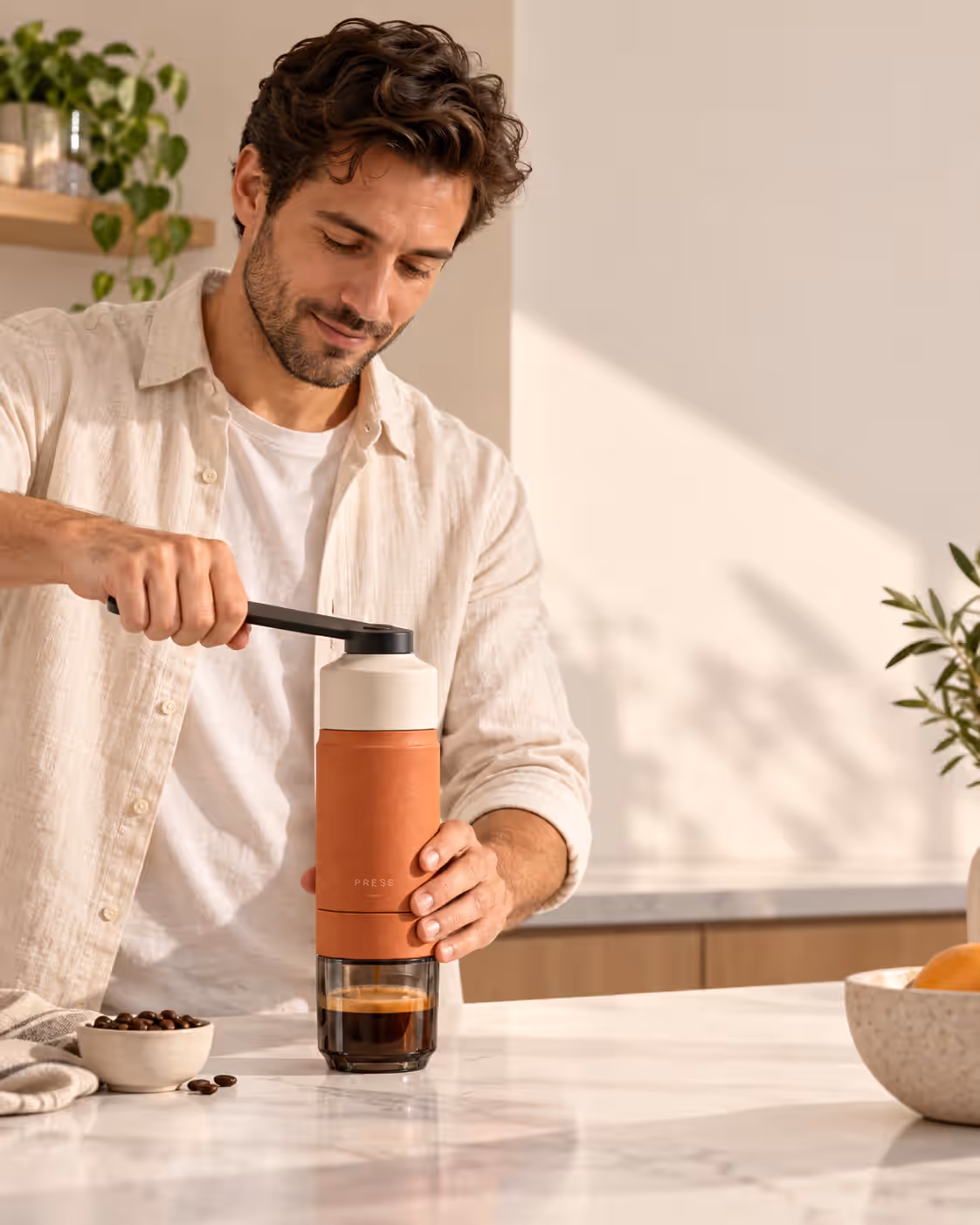 A man in a linen shirt pressing a shot from the espresso maker at a kitchen counter