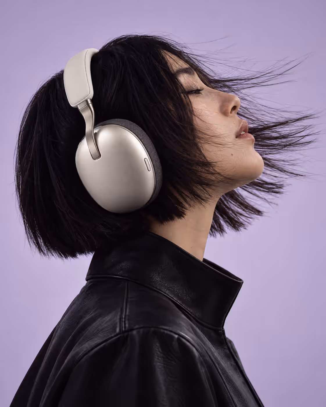 A woman in profile wearing the headphones, hair blown back against a lilac backdrop